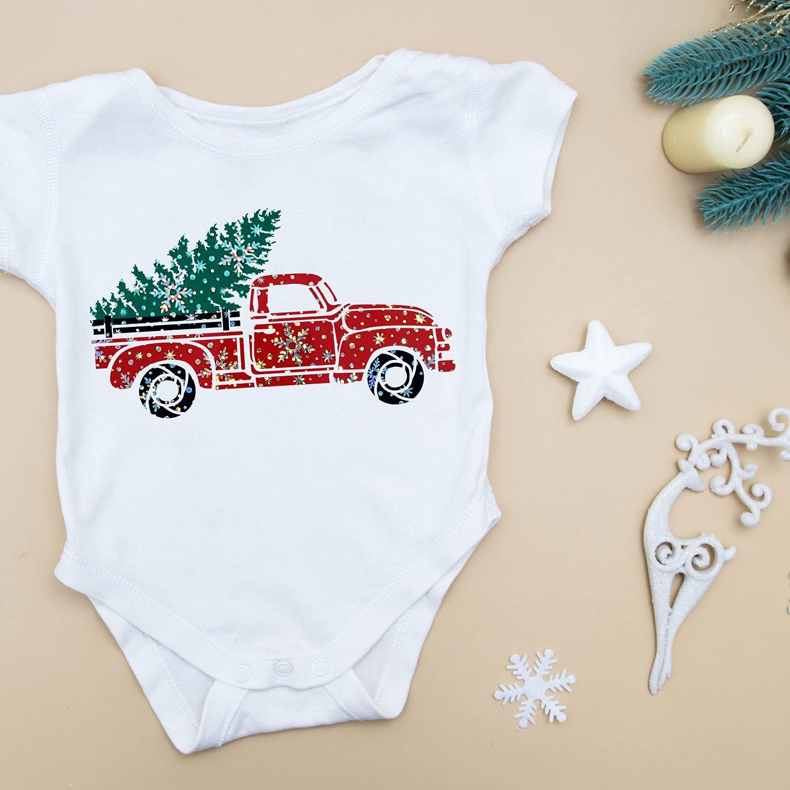 White baby bodysuit with a Christmas red truck and tree graphic, flat lay with festive decorations.