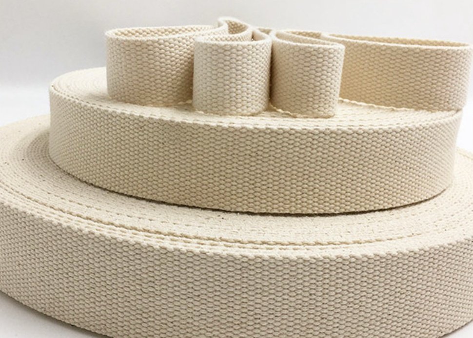 Three rolls of natural cotton webbing, one large and two smaller, stacked and coiled on a white background.