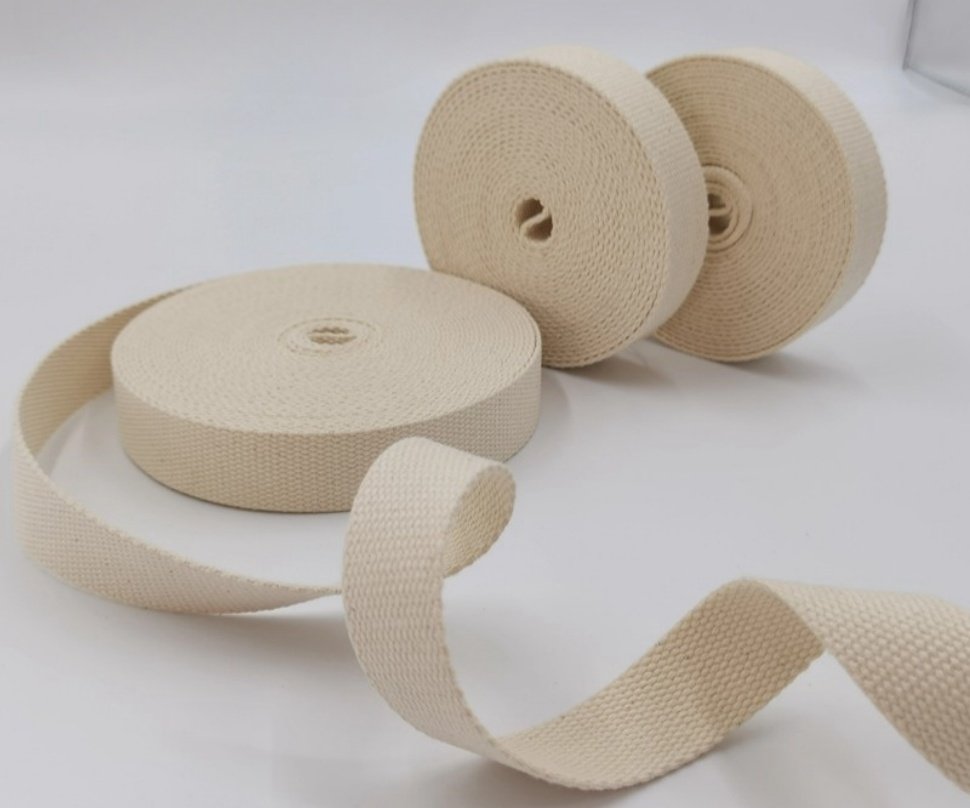Three rolls of natural cotton webbing, one unspooling, on a white background.