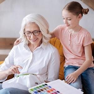 Grandmother and granddaughter doing embroidery together, with a box of colorful embroidery floss in the foreground.