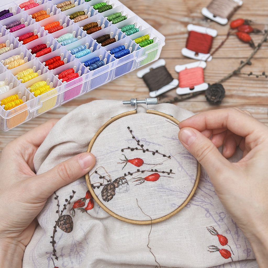 Hands embroidering a floral pattern with colorful thread spools and organizer box nearby
