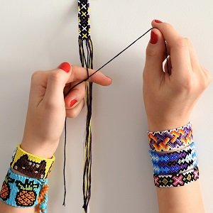 Hands creating a friendship bracelet with colorful embroidery floss, several finished bracelets visible on wrists.