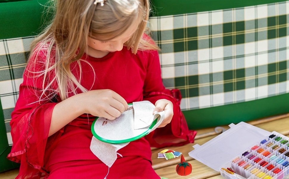 Young girl in red dress doing embroidery with colorful thread kit and organizer box