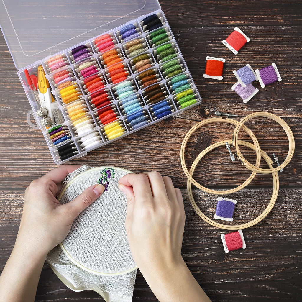 Hands cross-stitching with colorful embroidery floss kit and organizer box on wooden background