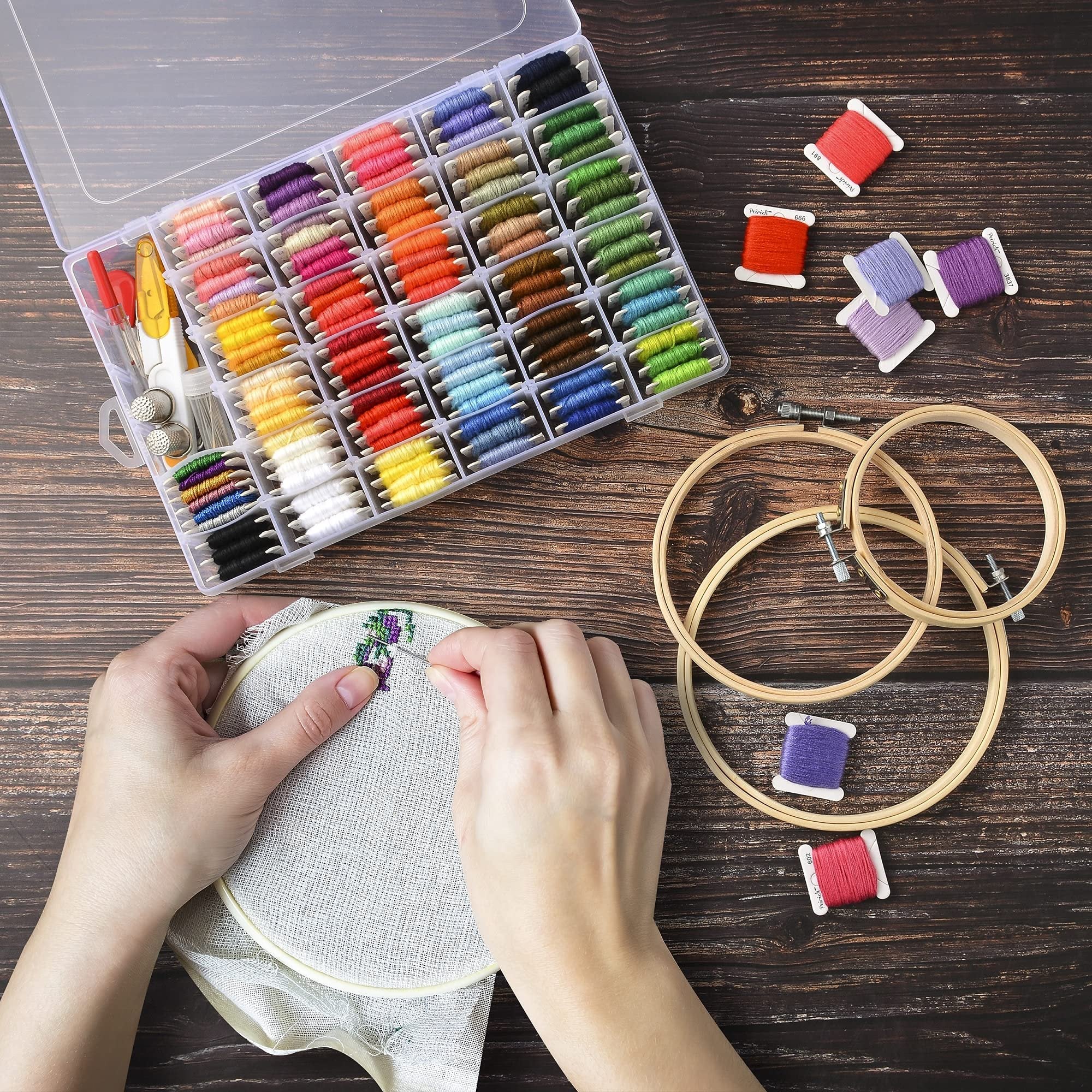 Hands cross-stitching with colorful embroidery floss kit and organizer box on wooden background