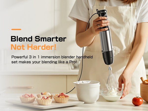 Person holding a silver immersion blender with whisk attachment, whipping cream in a bowl. Desserts on a tray in foreground.