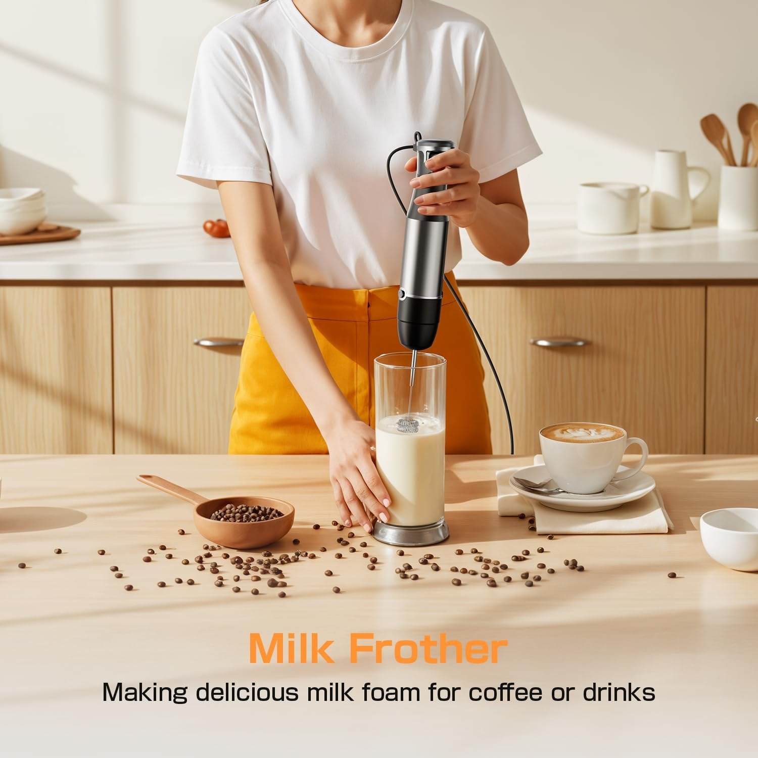 Person using a silver immersion blender to froth milk in a glass, with coffee and scattered beans on a wooden table.