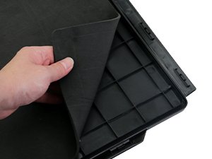 Hand lifting black rubber mat from black plastic tray with grid compartments