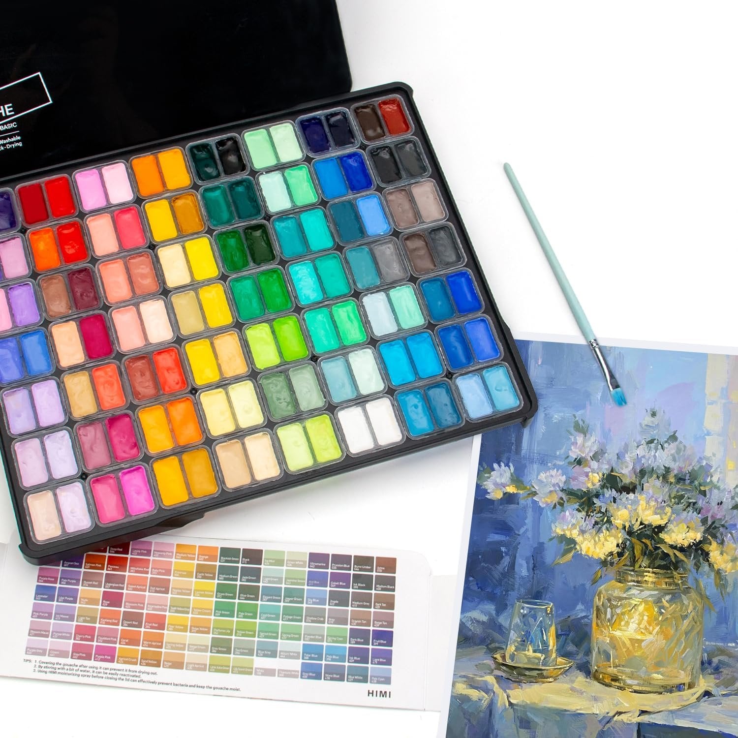 112-color gouache paint set with a brush and color chart, laid out on a table with a painting of flowers in a vase.