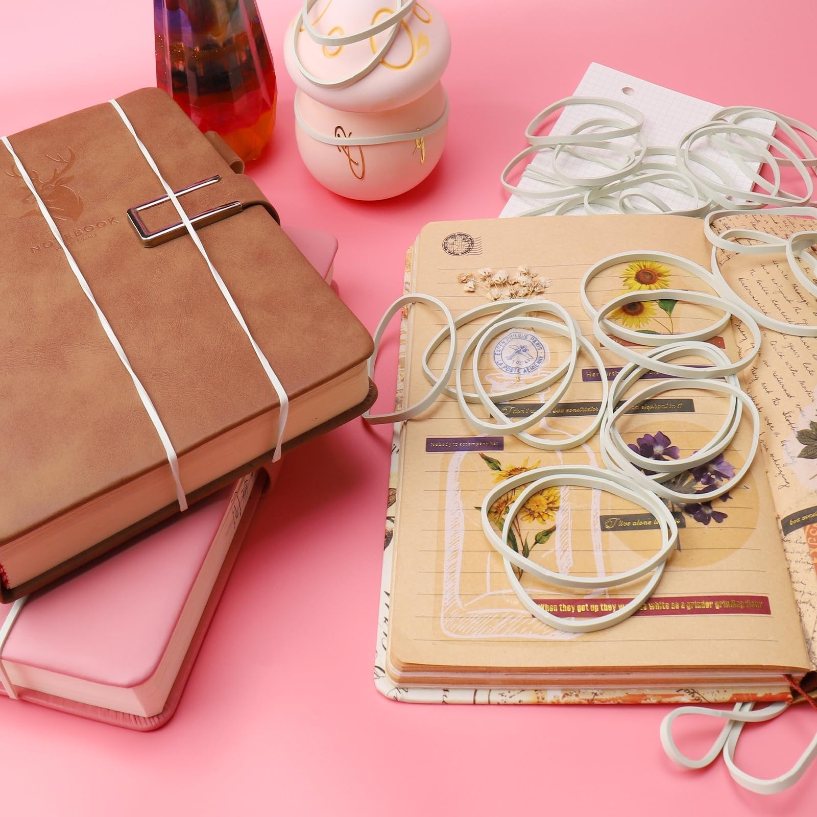 Light green rubber bands scattered on open notebooks with floral and vintage designs, alongside decorative pink and brown notebooks.