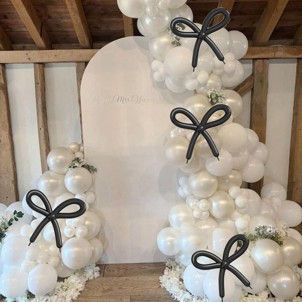 Pearl white balloon arch with black bow accents and a white arch backdrop with text