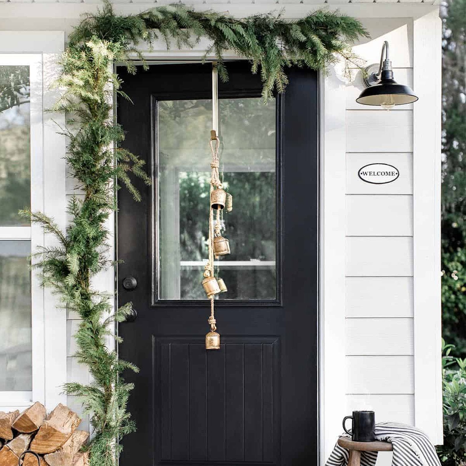 Front door decorated with evergreen garland and hanging bells, with a welcome sign on the siding.