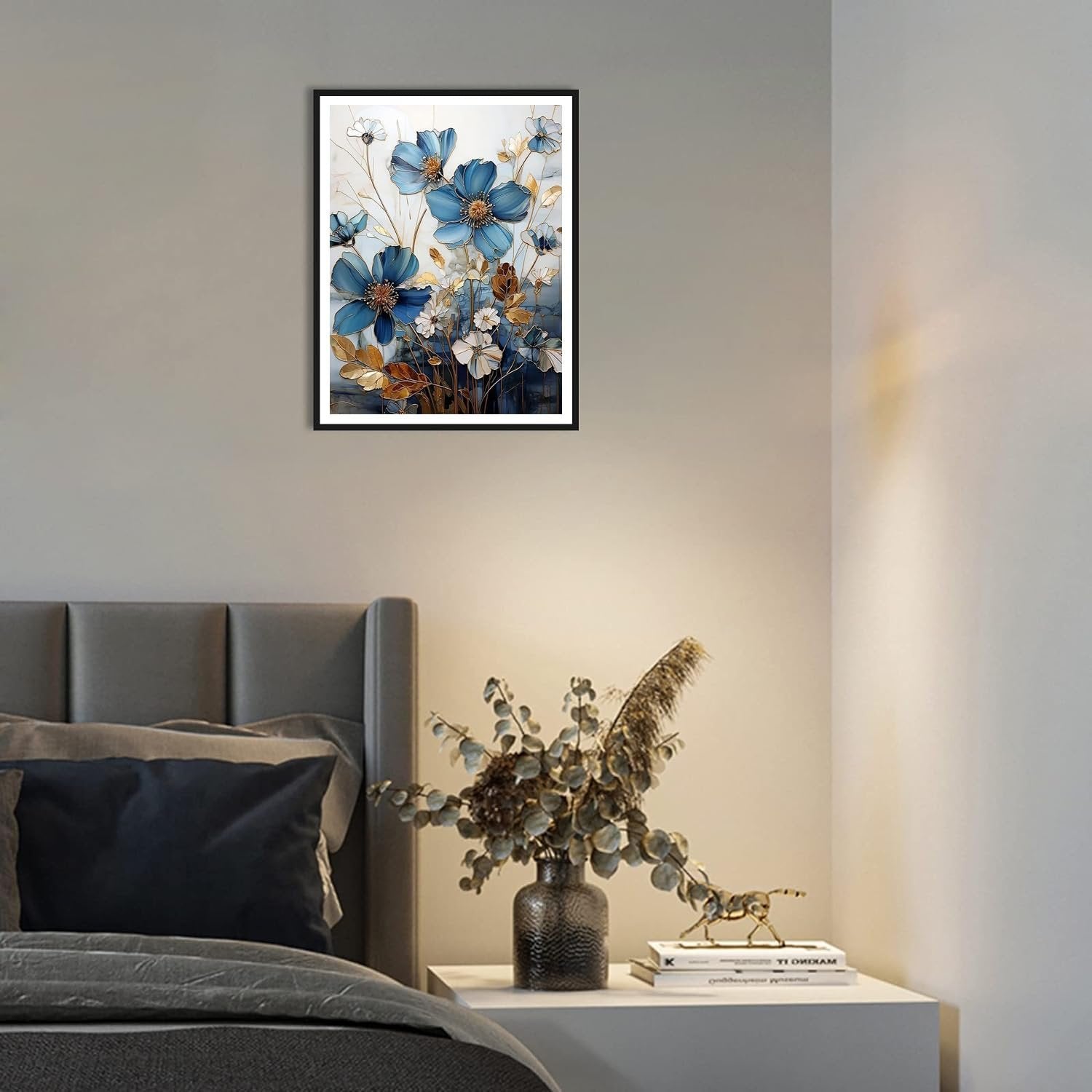 Framed blue floral artwork hanging above a bed with a nightstand and vase.