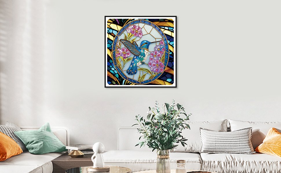 Framed 5D diamond painting kit featuring a blue hummingbird surrounded by purple flowers and a stained-glass-like background, displayed on a wall above a sofa.