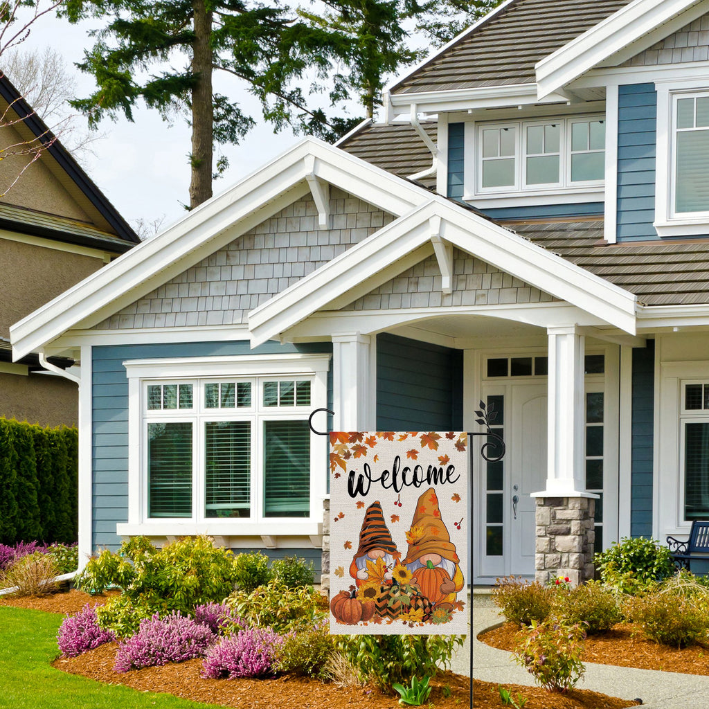 Fall garden flag with gnomes, pumpkins, and sunflowers displayed in front of a house.