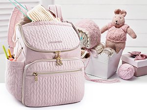 Pink quilted knitting backpack with yarn, needles, and a stuffed bunny.