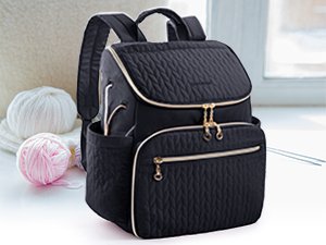 Black quilted knitting backpack with gold trim and zippers, shown with yarn and knitting needles.