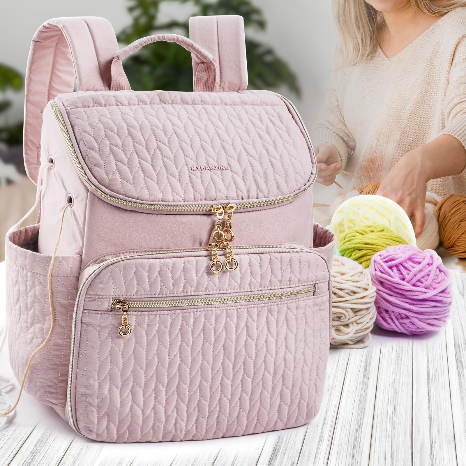 Pink quilted knitting backpack with gold zippers and charms, shown with yarn and a person knitting in the background.