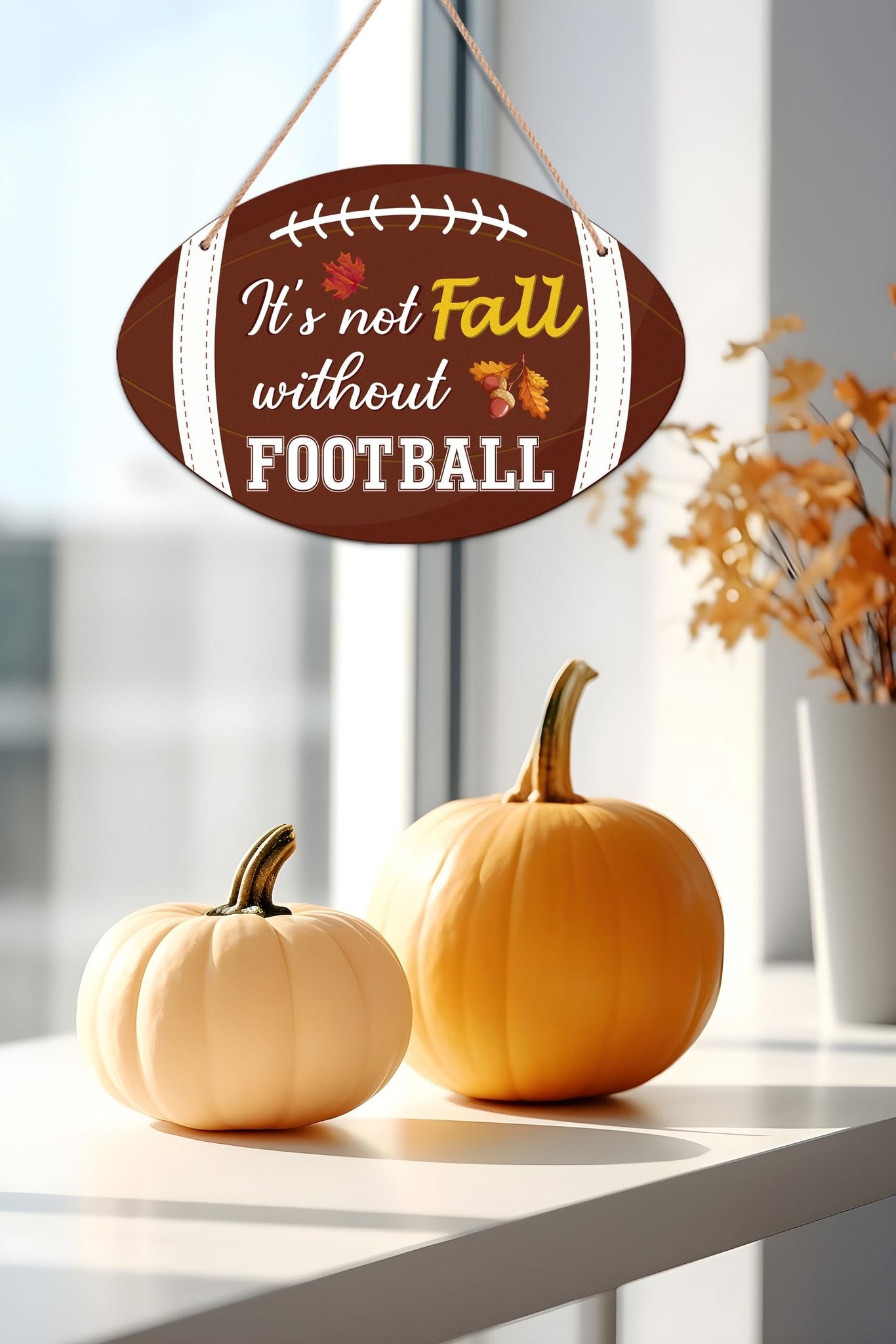 Football-shaped fall hanging sign with text 'It's not Fall without FOOTBALL', displayed with pumpkins and autumn leaves.