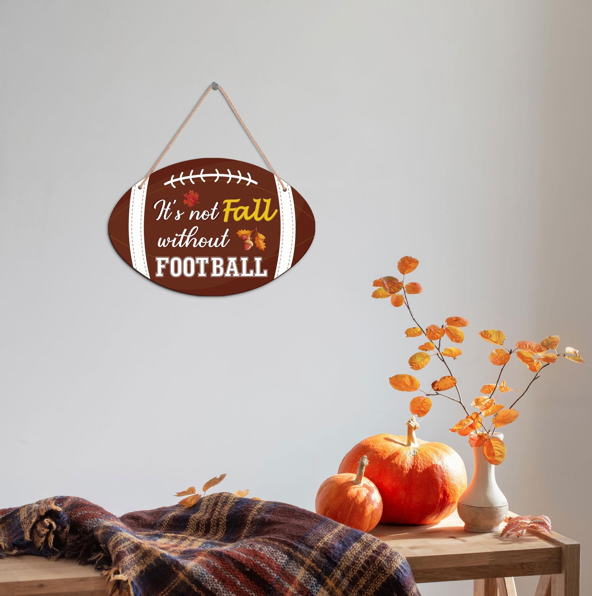 Oval wooden football-shaped fall hanging sign with text 'It's not Fall without FOOTBALL', displayed on a wall.