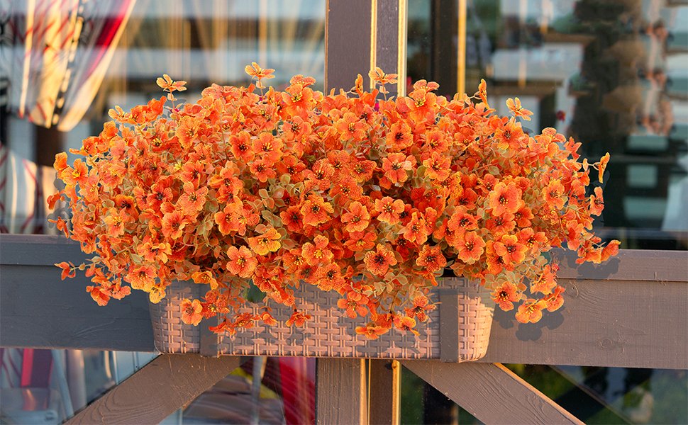Artificial orange flowers with eucalyptus leaves in a woven planter box, displayed outdoors.