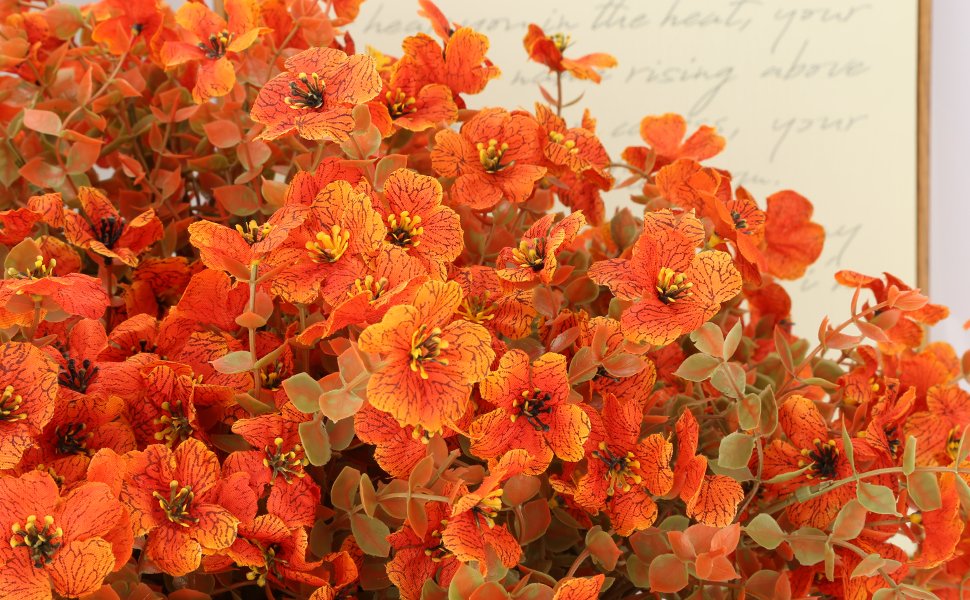 Close-up of artificial orange fall mums with green eucalyptus leaves, detailed petals and stamens.