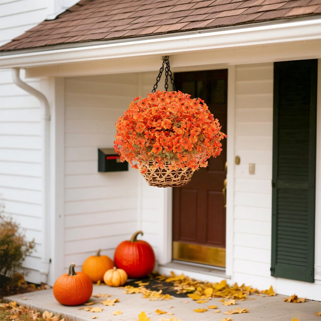 Hanging basket of orange artificial mums with eucalyptus leaves on a porch with pumpkins and fallen leaves
