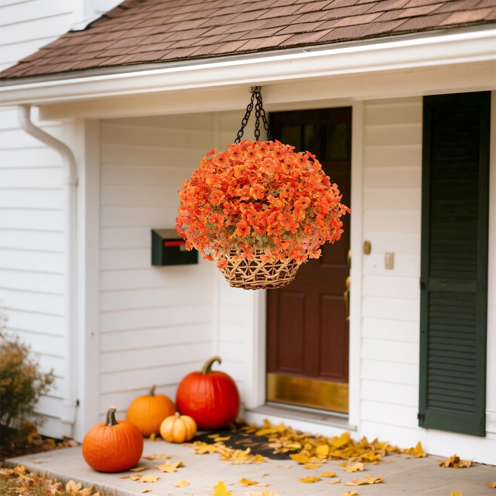 Hanging basket of orange artificial mums with eucalyptus leaves on a porch with pumpkins and fallen leaves
