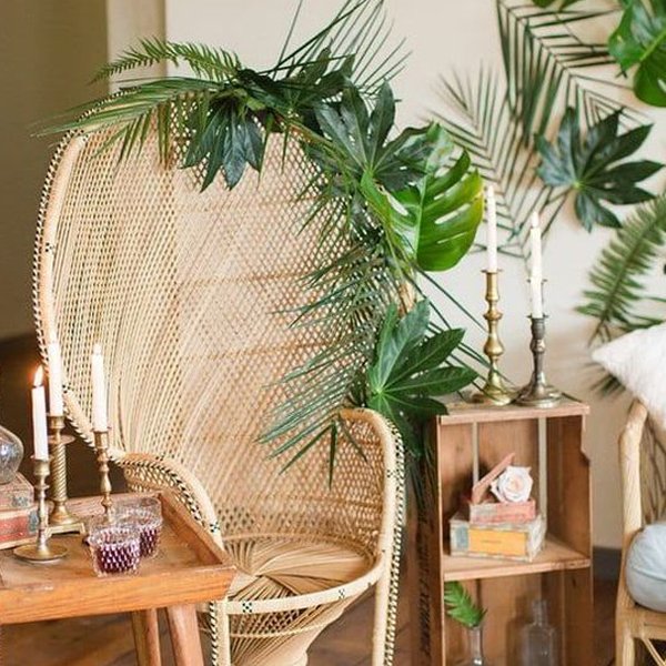 Artificial palm leaves draped over a wicker peacock chair with brass candlesticks and decorative items.