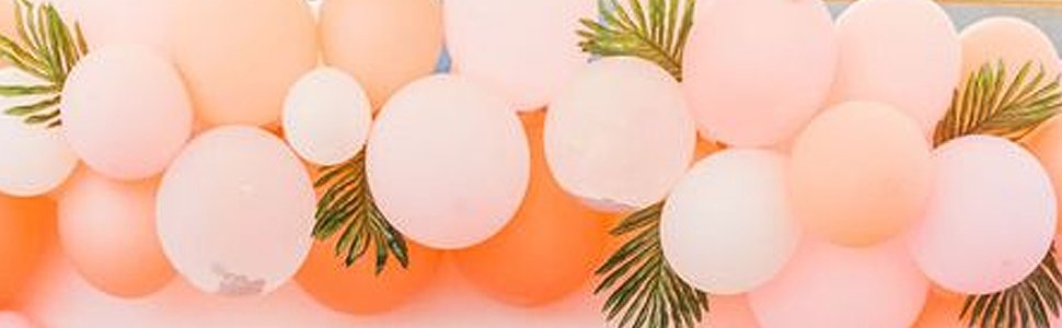 Close-up of a balloon garland with pastel pink, peach, and orange balloons interspersed with artificial palm leaves.