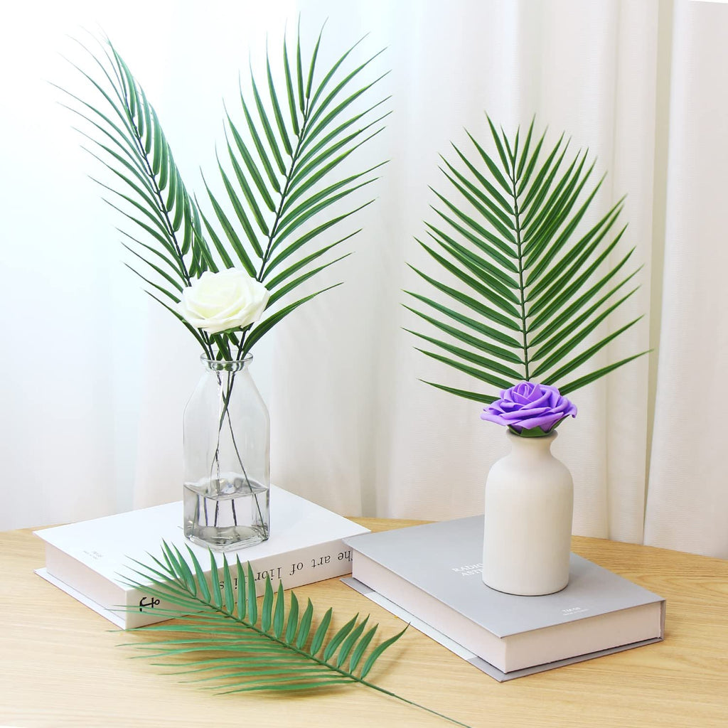 Artificial palm leaves in vases with roses on books, one leaf on table