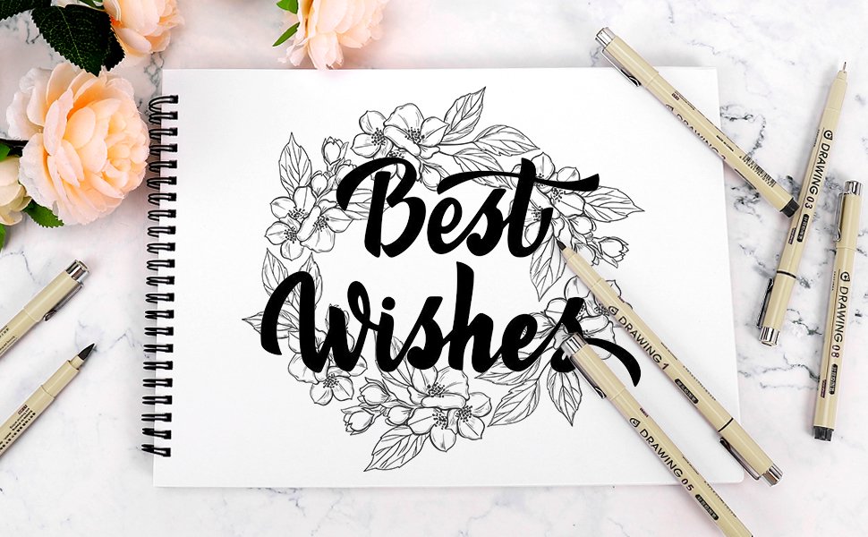 Drawing pens arranged around a sketchbook with a floral 'Best Wishes' design