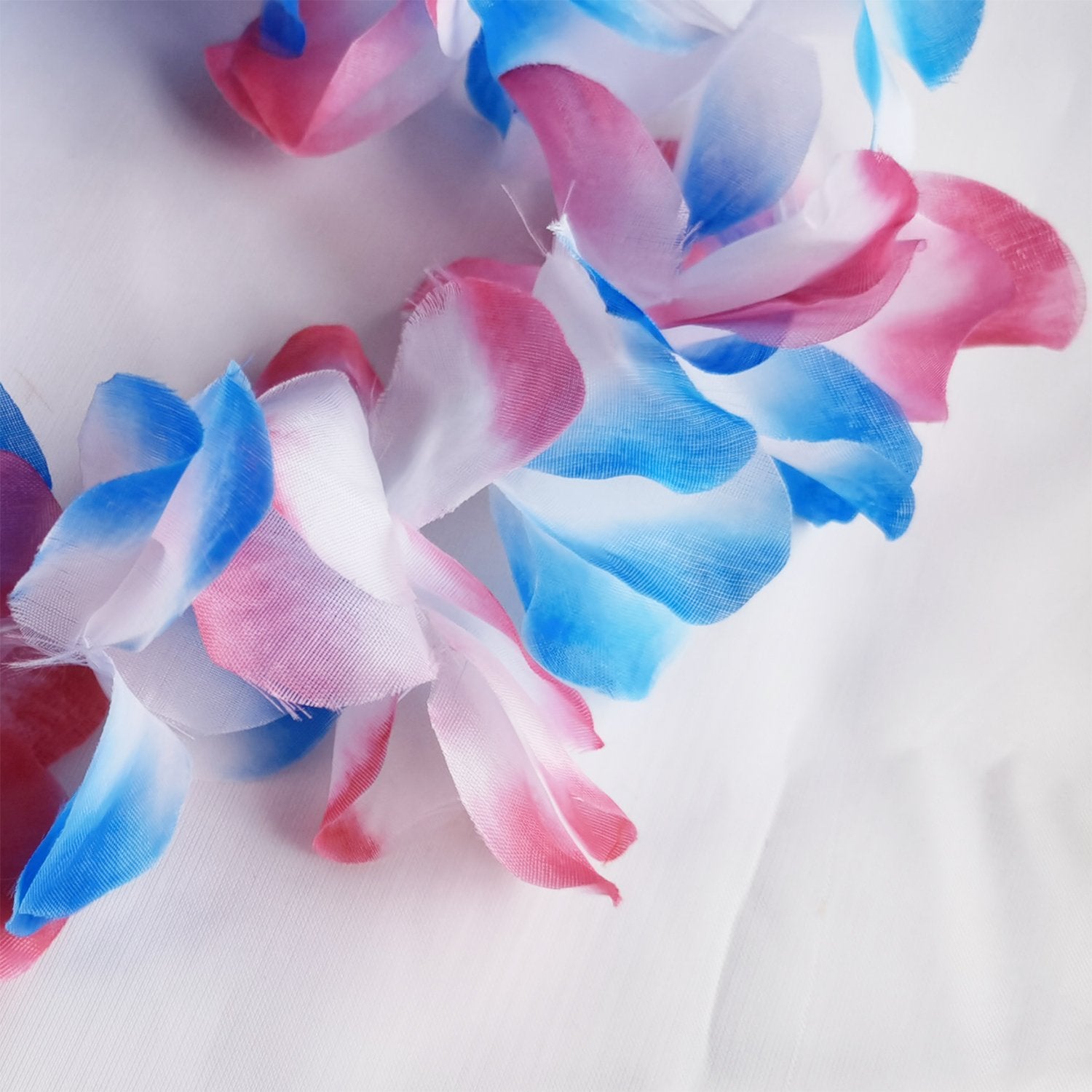 Close-up of a pink, white, and blue floral lei with green leaves on a white background.