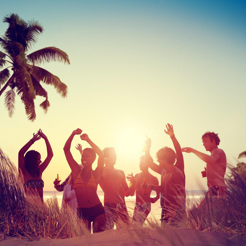 Group of diverse friends dancing on a beach at sunset with a palm tree