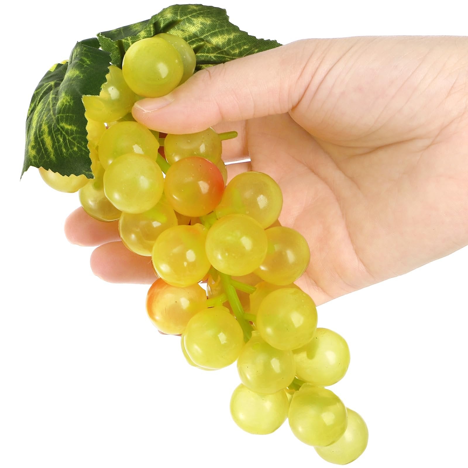 Hand holding a bunch of artificial green grapes with a leaf against a white background.