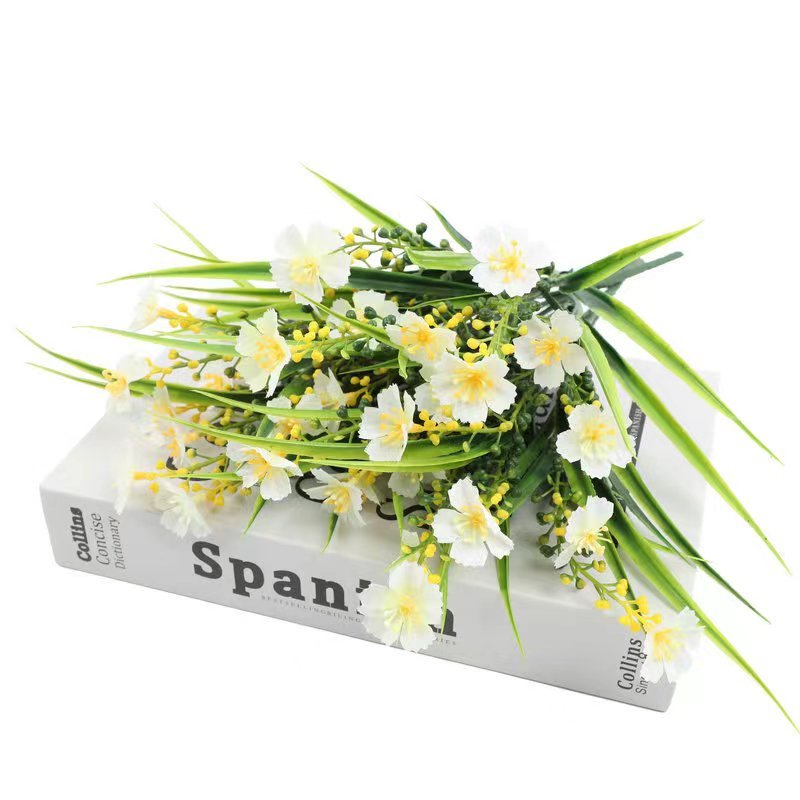 Artificial daisy flowers with green leaves and yellow buds arranged on a book