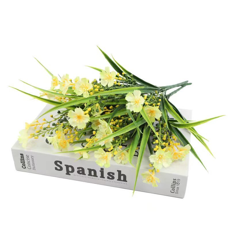 Artificial yellow daisy flowers with green leaves resting on a Spanish dictionary