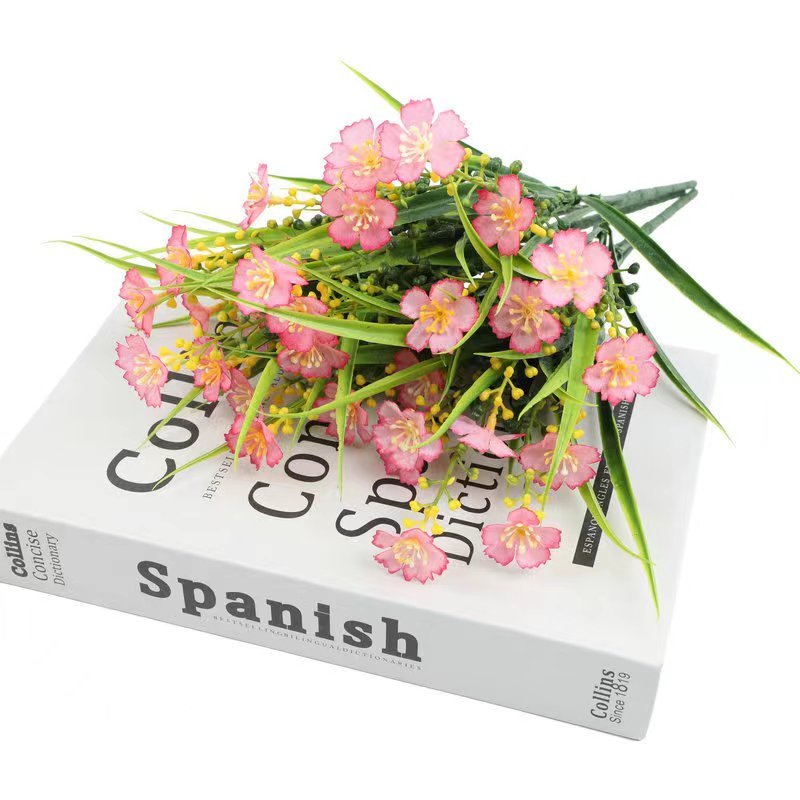 Artificial pink daisy flowers with green leaves resting on a Spanish dictionary.