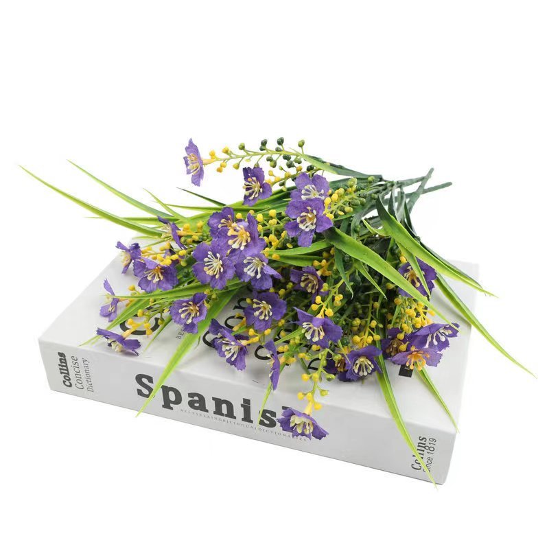 Artificial purple daisy flowers with yellow buds and green leaves resting on a Spanish dictionary.