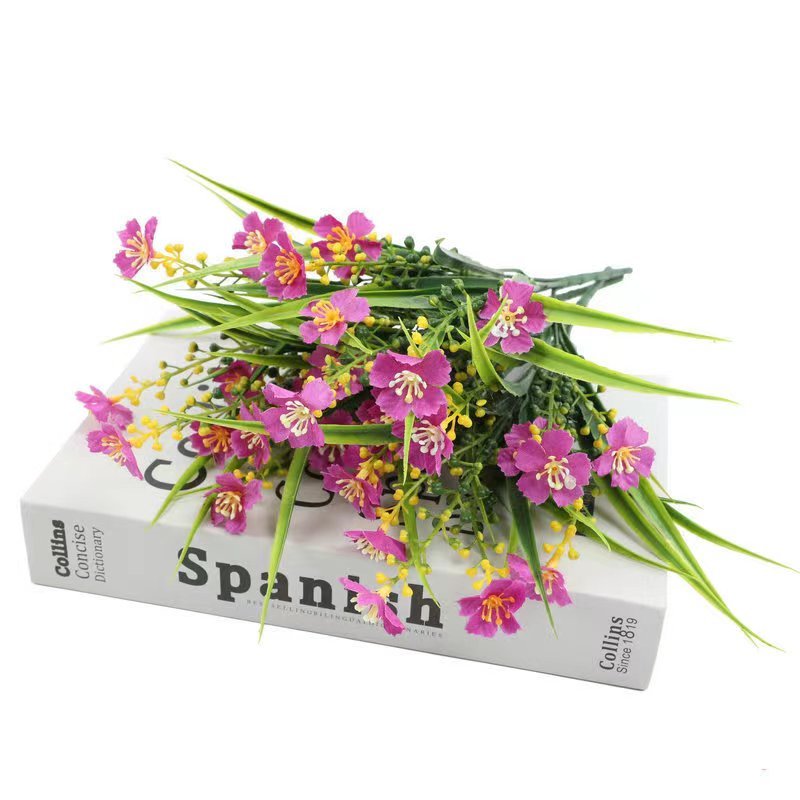 Artificial purple daisy flowers with green leaves resting on a book