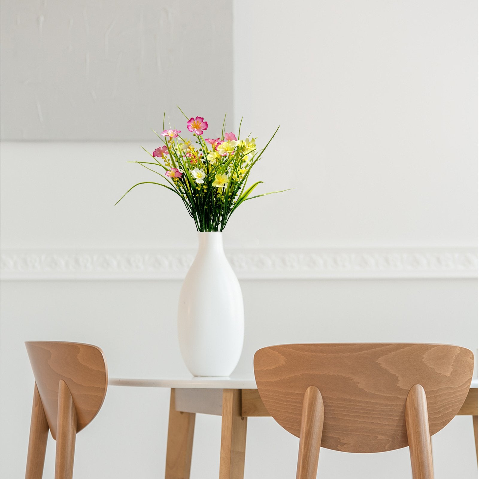 Artificial daisy flowers in a white vase on a table with wooden chairs