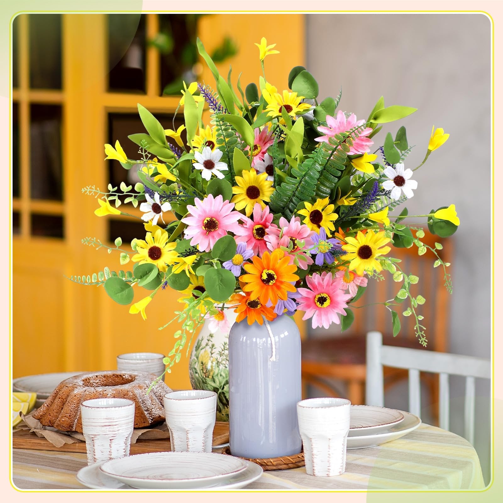 Vase of multicolor artificial daisy wildflowers on a table with a bundt cake and place settings