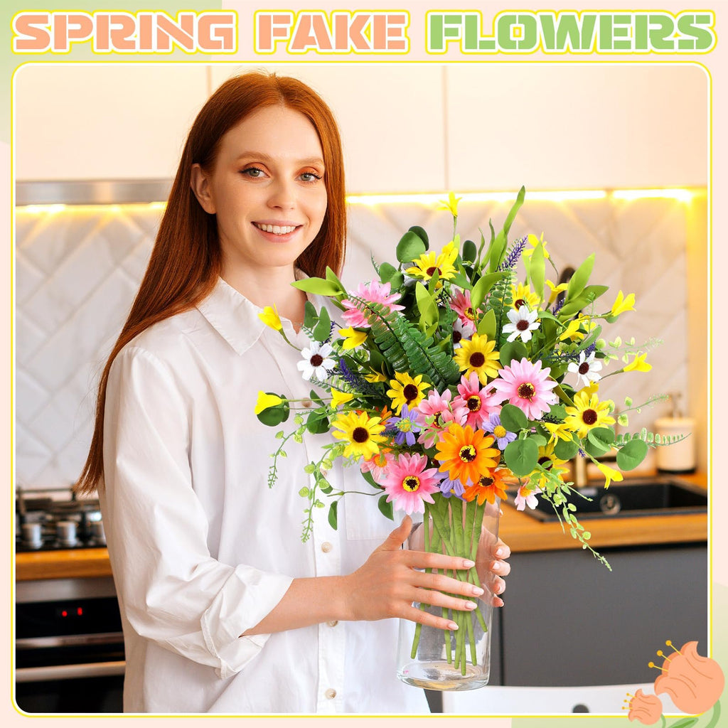 Woman holding a clear vase filled with multicolor artificial daisy wildflowers and greenery