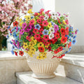 Multicolor artificial daisy flowers in a decorative urn on a marble surface with a blurred pink tree in the background.