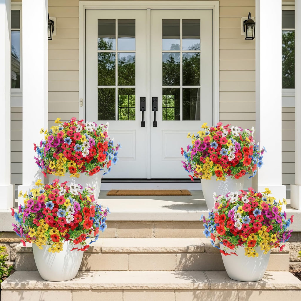 Four white planters filled with multicolor artificial daisy flowers on a porch with double doors.
