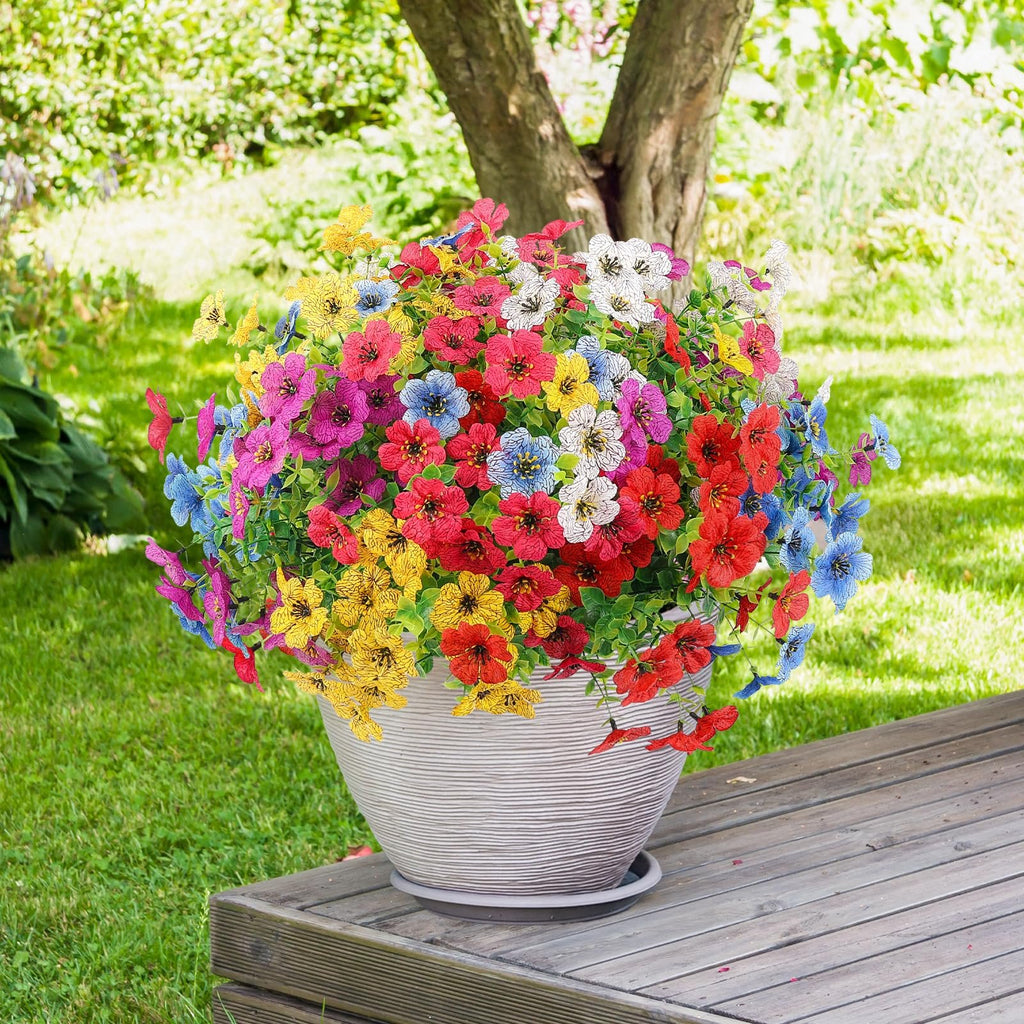 Bundle of multicolor artificial daisy flowers in a textured pot on a wooden deck with a garden background