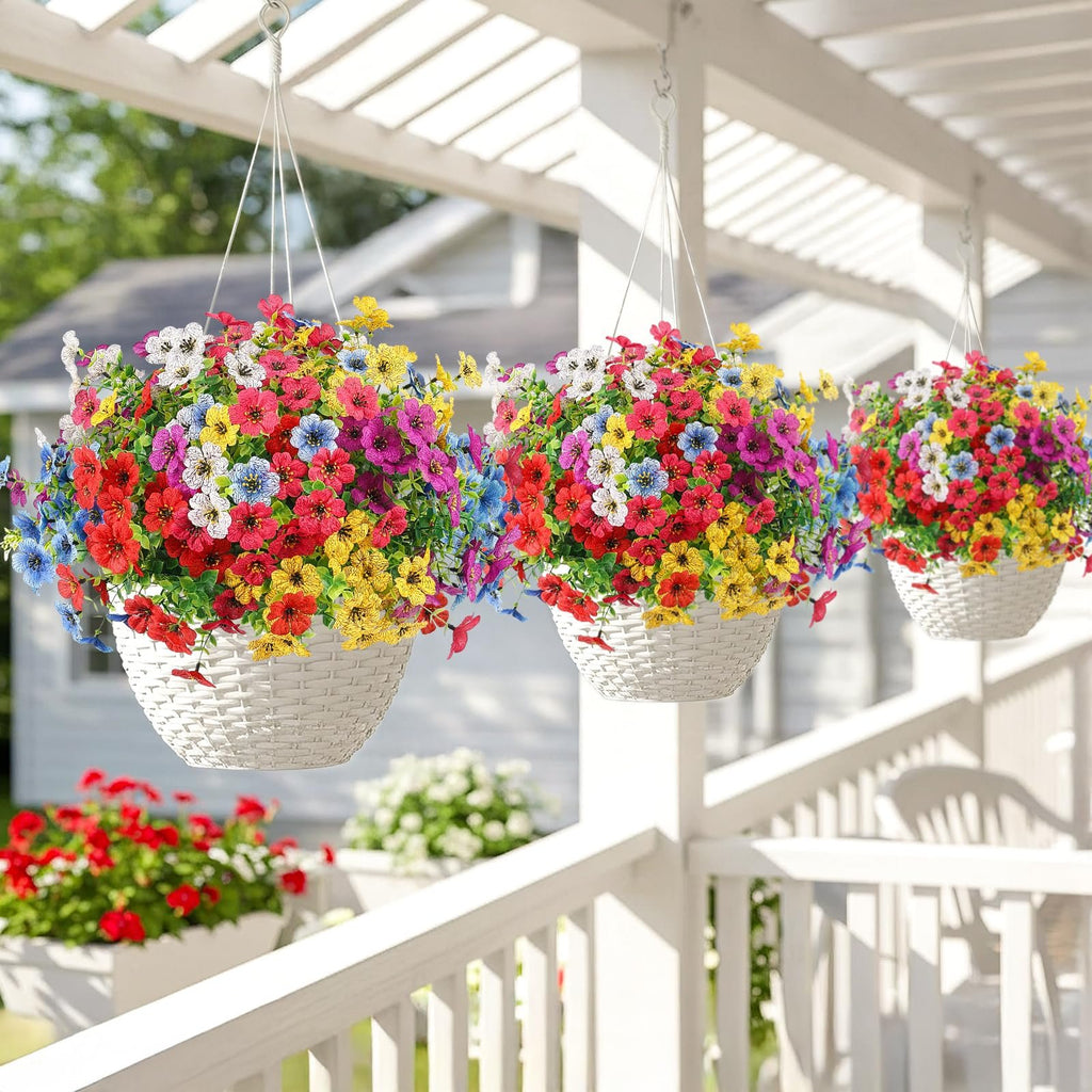Three hanging baskets overflowing with multicolor artificial daisy flowers, displayed on a white porch railing.