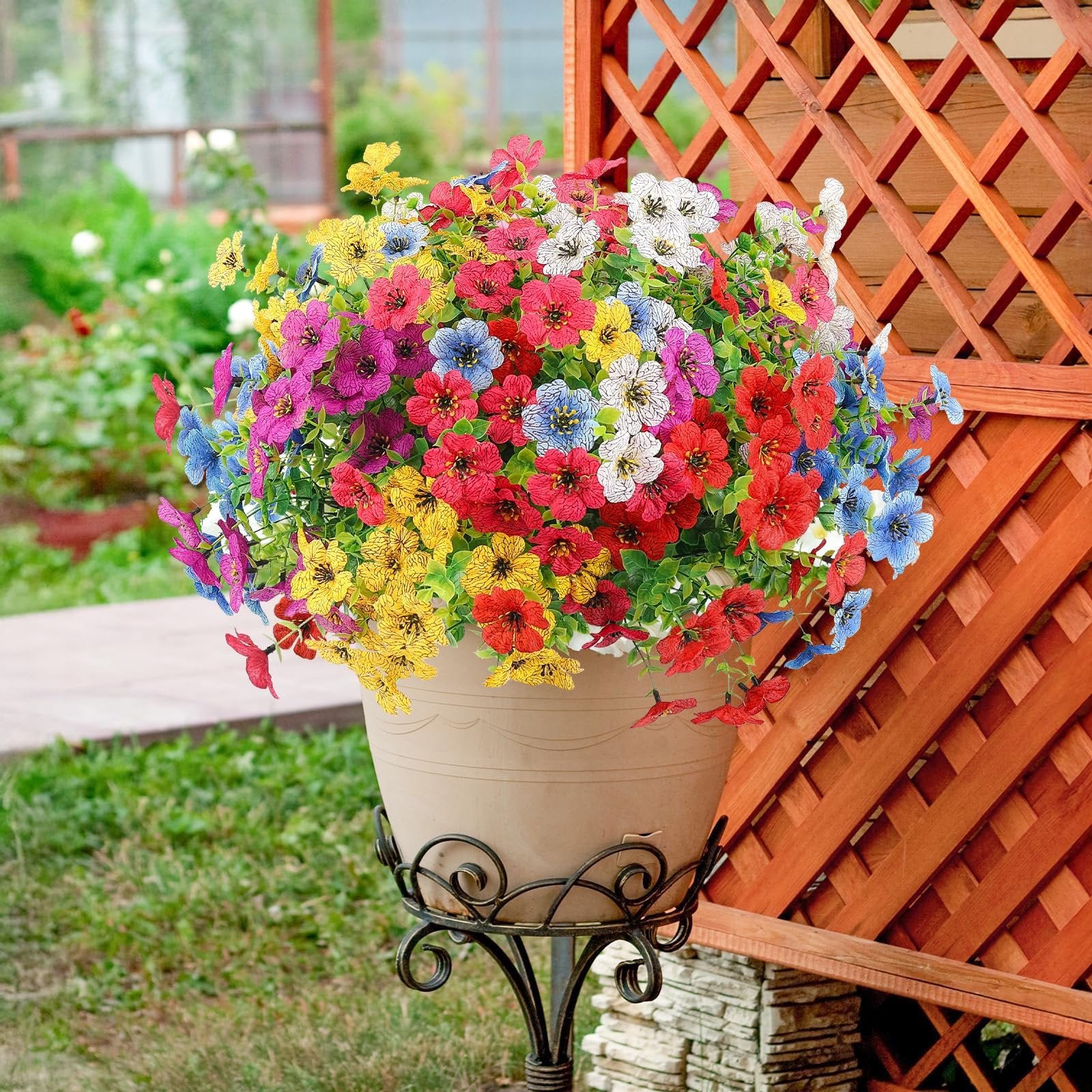 Multicolor artificial daisy flowers in a pot on a stand, displayed outdoors next to a wooden lattice.