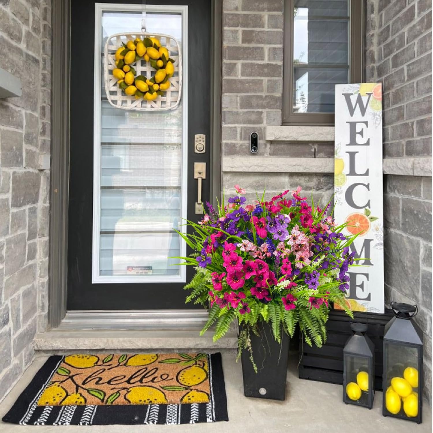 Front door entryway with a large bouquet of artificial flowers in a black planter, a lemon-themed doormat, and a welcome sign.
