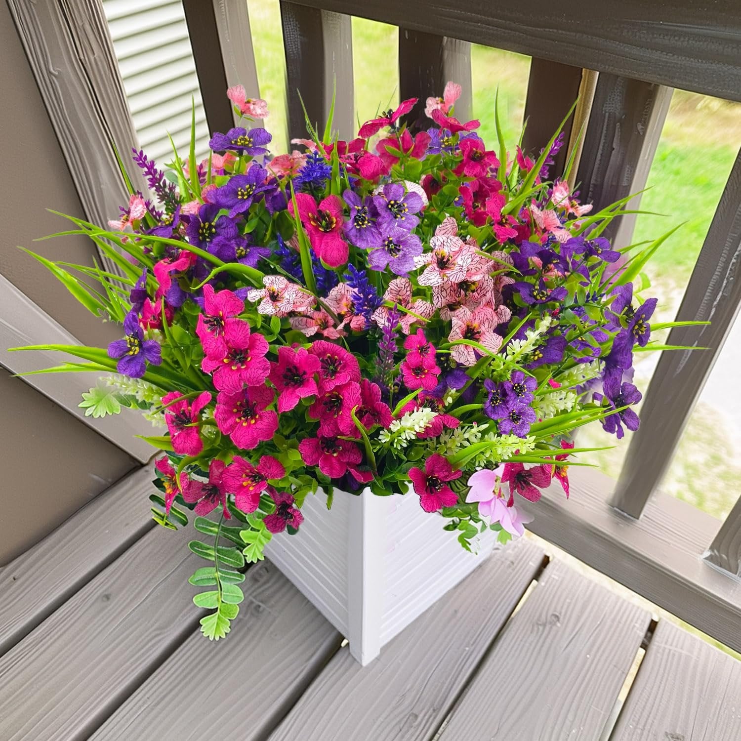 Mixed color artificial flowers in a white planter on a wooden deck railing